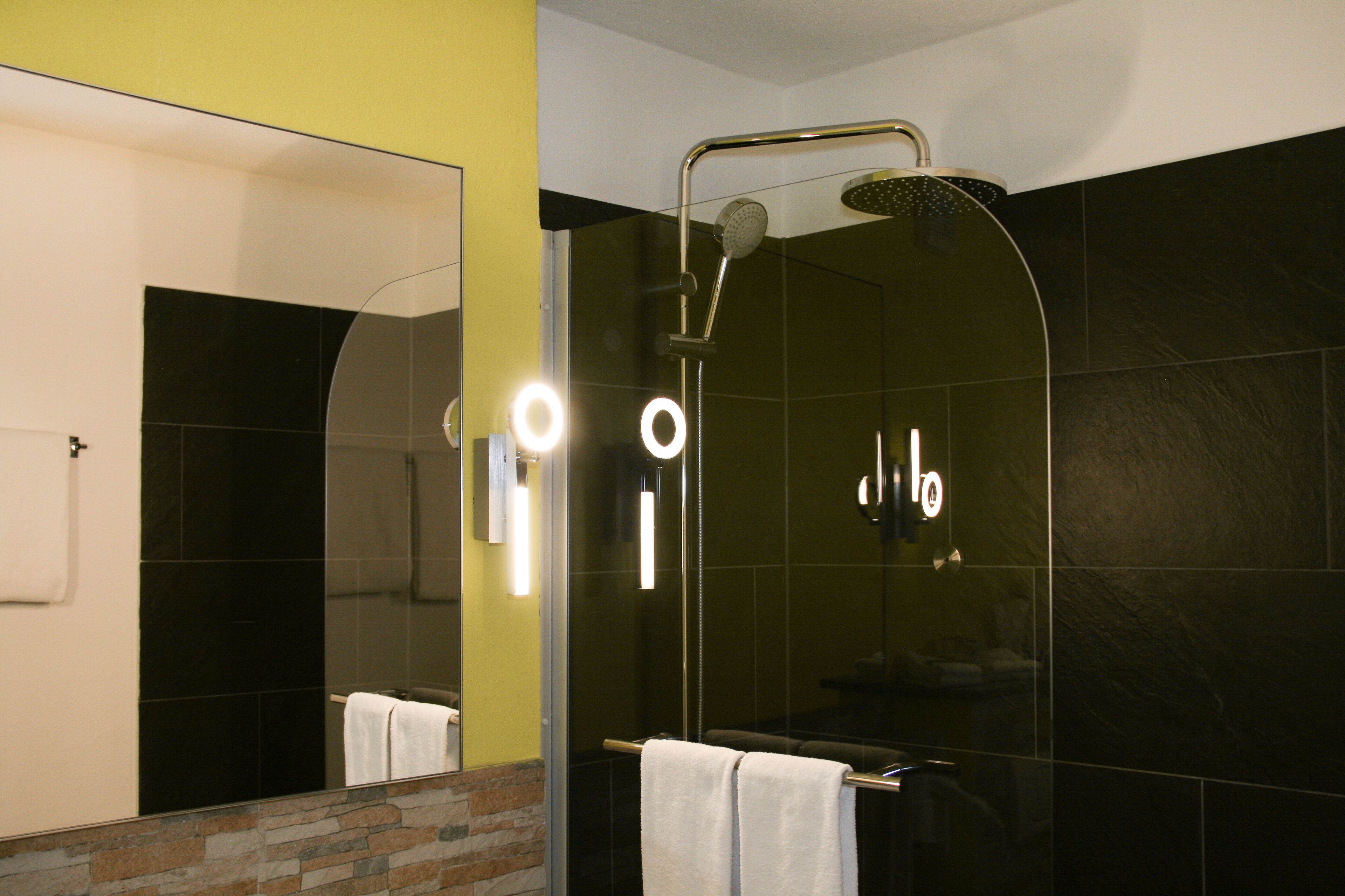A modern bathroom with a glass-enclosed shower, a visible towel rack, and a mirror with lights.
