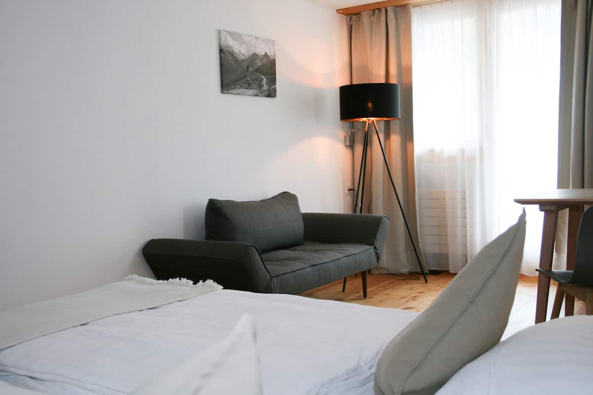 A hotel room with a bed, a sofa, a small table, a lamp, and a picture on the wall.