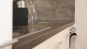 A kitchen with a dark countertop, a coffee maker, and a glass vase. - Hotel Solaria (Surses)