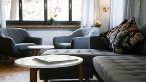 A modern living room with a grey sofa, two armchairs, a round coffee table, and a window with curtains. - Hotel Solaria (Surses)