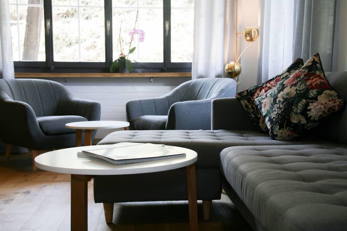 A modern living room with a grey sofa, two armchairs, a round coffee table, and a window with curtains.