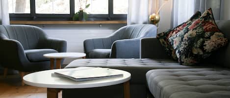 A modern living room with a grey sofa, two armchairs, a round coffee table, and a window with curtains.