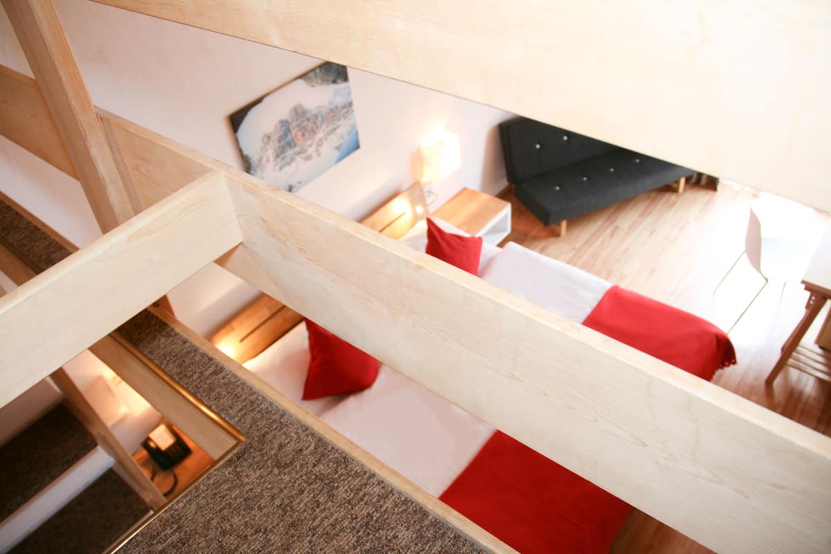 A modern interior with a wooden staircase, a sofa with red cushions, a small table, and a painting on the wall.