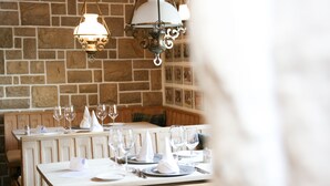 A restaurant with wooden tables and benches, stone walls, and hanging light fixtures. - Hotel Solaria (Surses)