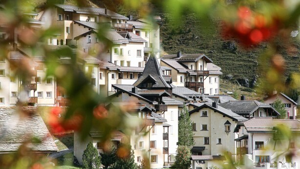 A cluster of multi-story buildings with balconies, set against a hillside backdrop. - Hotel Solaria (Surses)