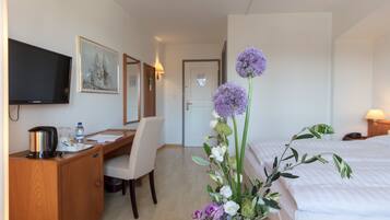 Une chambre d’hôtel comprenant un lit, un bureau avec une chaise, une télévision et un arrangement floral.