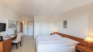 A hotel room with a bed, bedside table, lamp, desk with chair, TV, and artwork on the walls.