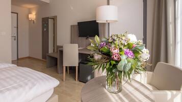 Une chambre d’hôtel comprenant un lit, un bureau, une chaise, une télévision, une lampe et un vase avec des fleurs.