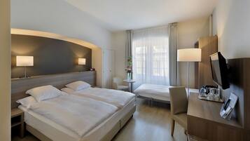 A hotel room with two beds, a desk with a TV, and a small table with a vase of flowers.