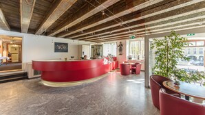 Un área de recepción con mostrador rojo, mobiliario moderno y un techo decorativo.