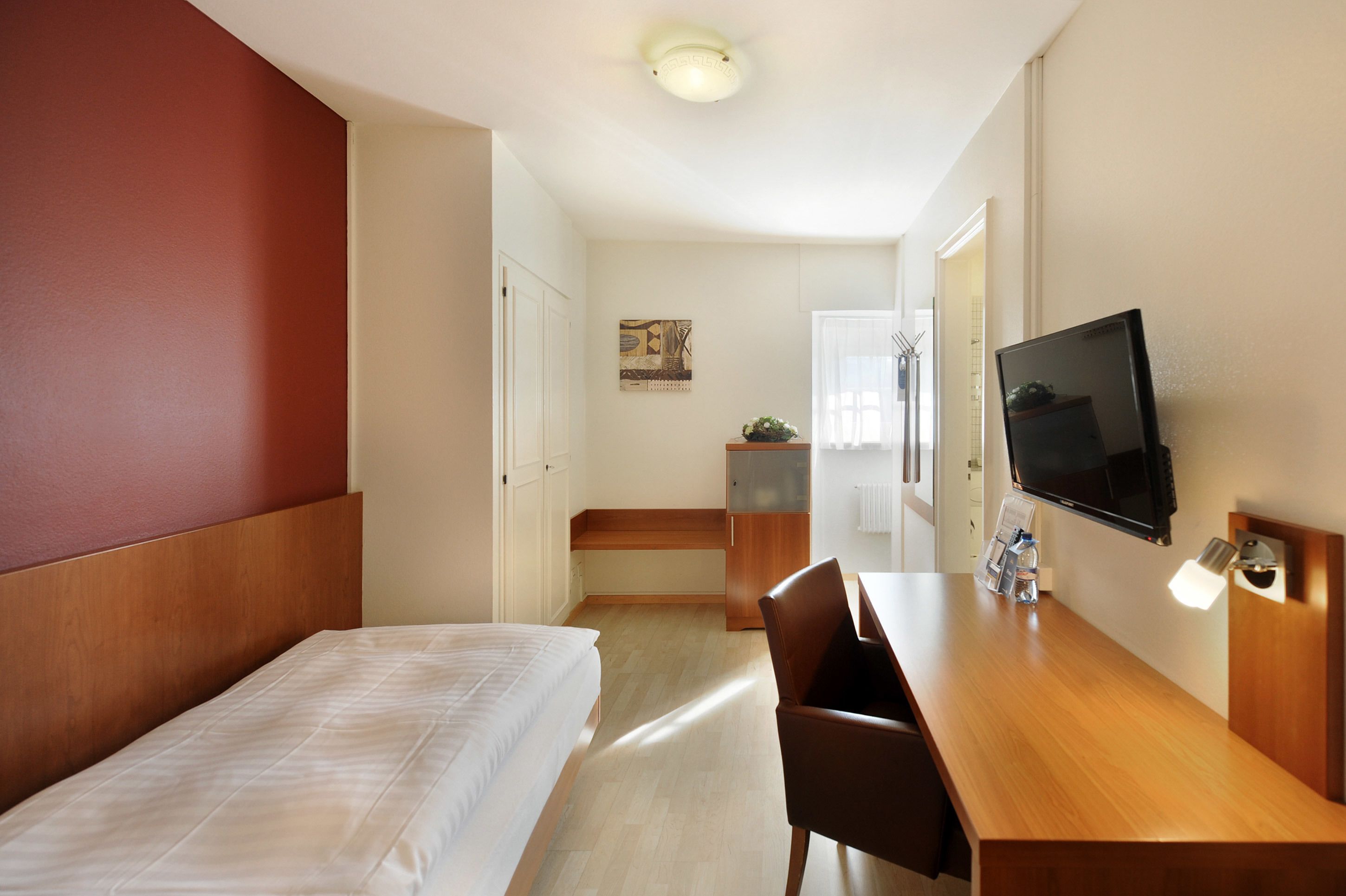 Habitación de hotel con cama, escritorio, silla, televisor y una pequeña cocina.