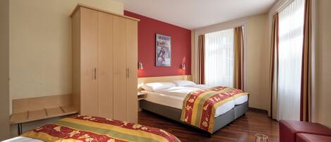 A hotel room with two beds, a wardrobe, a desk with a chair, and a window with curtains.