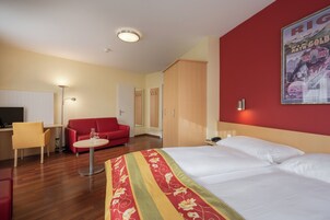 Quarto de hotel com cama, sofá vermelho, escrivaninha e cadeira.