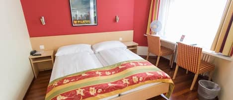 Habitación de hotel con cama, escritorio, silla, un cartel en la pared y ventana con cortinas.