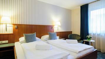 Ein Hotelzimmer mit Doppelbett, zwei Nachttischlampen, einem kleinen Tisch mit einer Vase und einem Sessel.