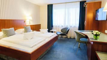 Une chambre d’hôtel avec un grand lit, un bureau, une chaise, une télévision et une fenêtre avec des rideaux.