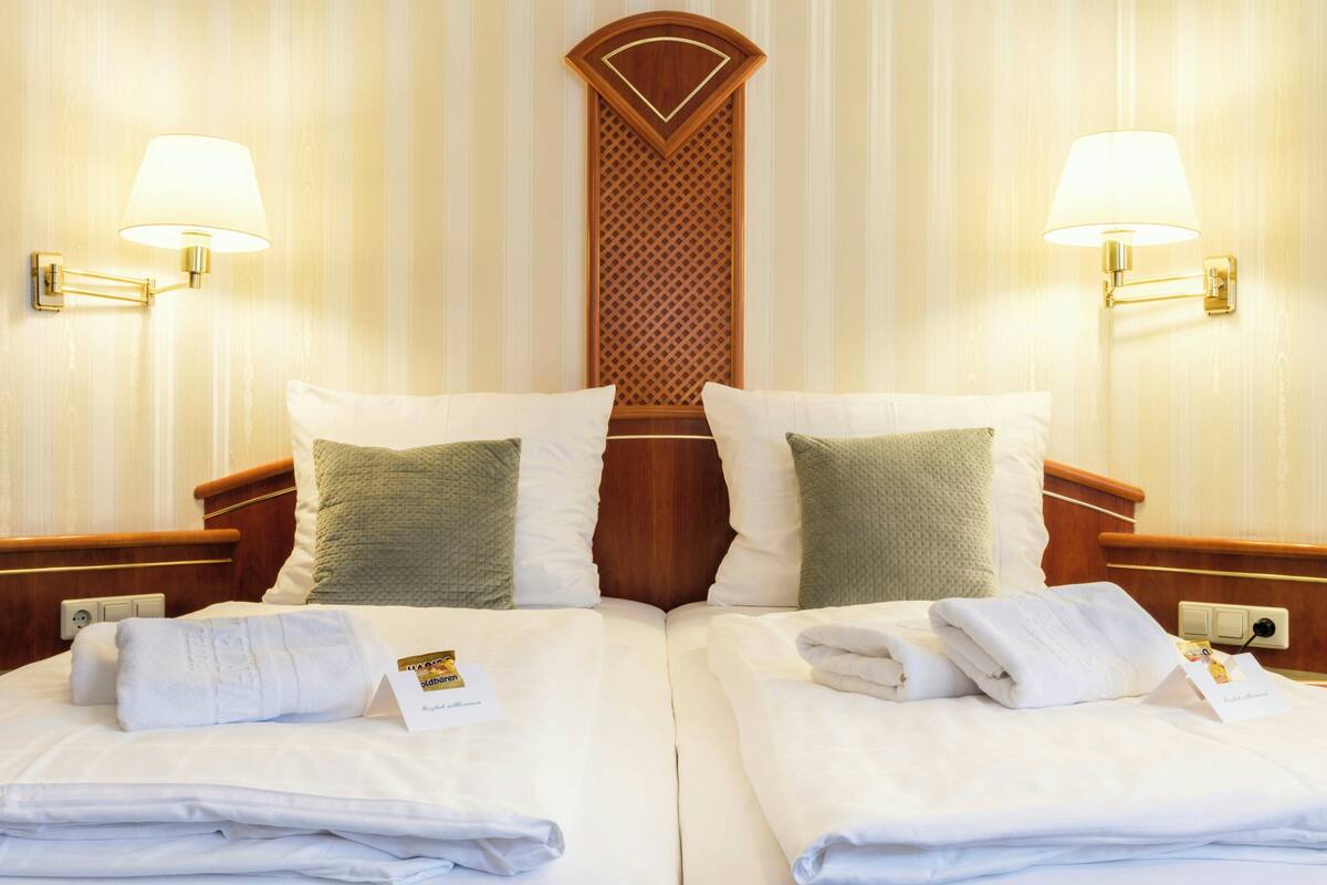 Een hotelkamer met twee bedden, elk voorzien van een kussen, nachtkastje en lamp.