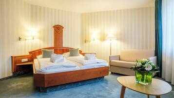 Una habitación de hotel con una cama de madera, dos lámparas de noche, un sofá y una mesita con un jarrón de flores.