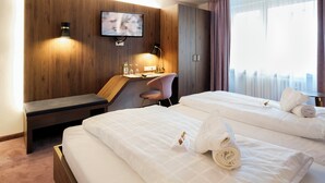 A hotel room with two beds, a desk, a bench, a TV, and a city view. - TOP VCH Hotel Wartburg Stuttgart (Stuttgart)
