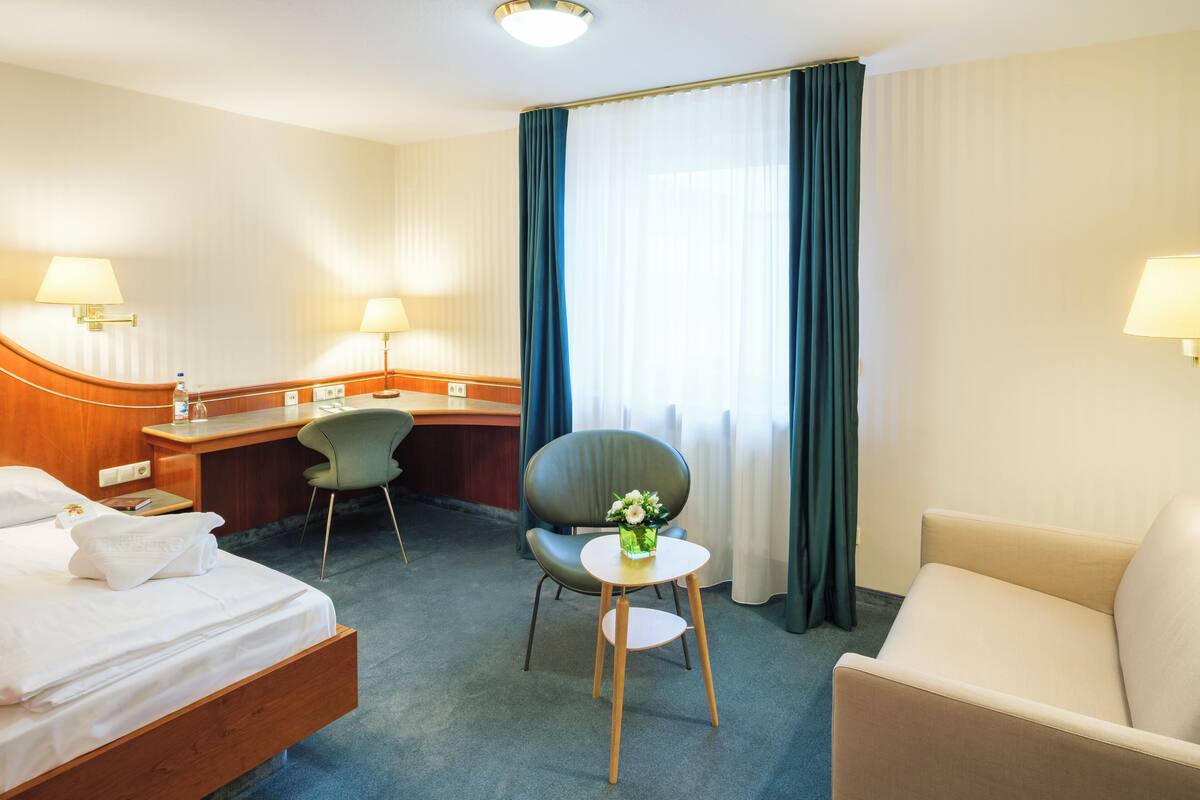 Een hotelkamer met een bed, een bureau, een stoel, een kleine tafel met een vaas en een bank.
