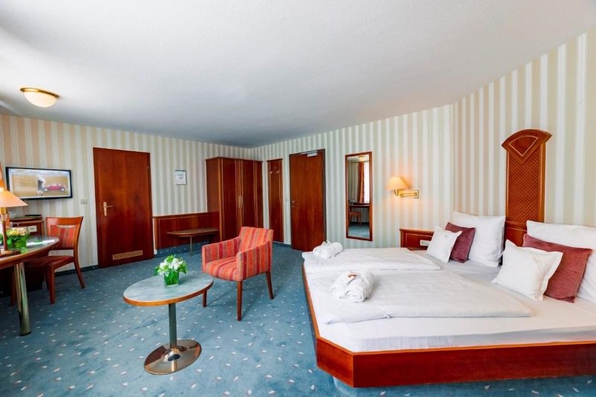 A hotel room with a bed, a desk, a chair, a small table, and a mirror.
