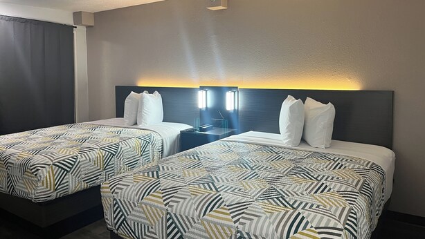 Ein Hotelzimmer mit zwei Betten, jeweils mit einem Bettbezug mit geometrischem Muster, einer dunklen Kopfteil und einem Nachttisch mit Lampe.