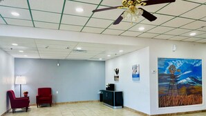 Eine geräumige Lobby mit Fliesenboden, einem Empfangstresen, einem roten Sessel, einem schwarzen Schrank und einem Deckenventilator.