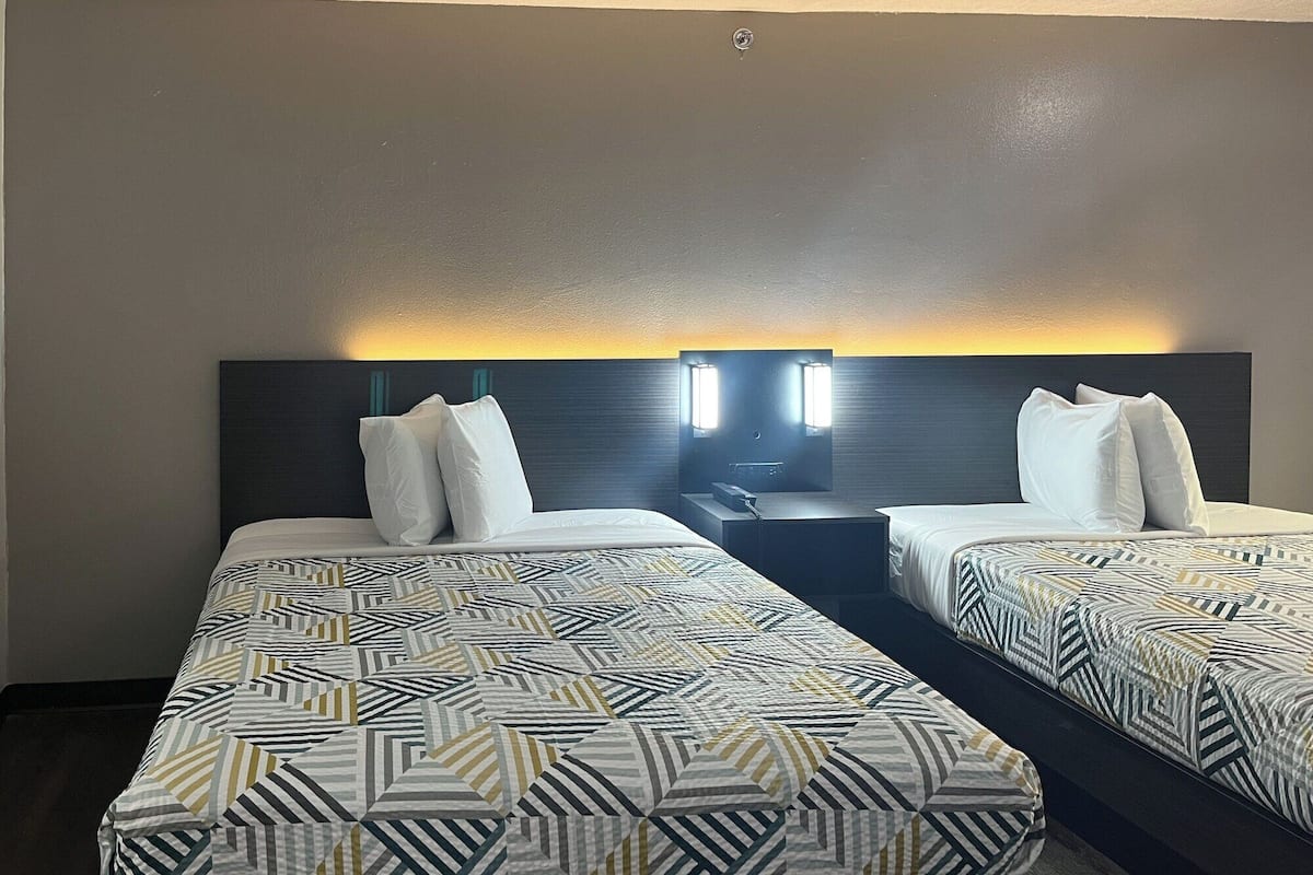 A hotel room with two beds, each with patterned bedding and a headboard with integrated lighting.