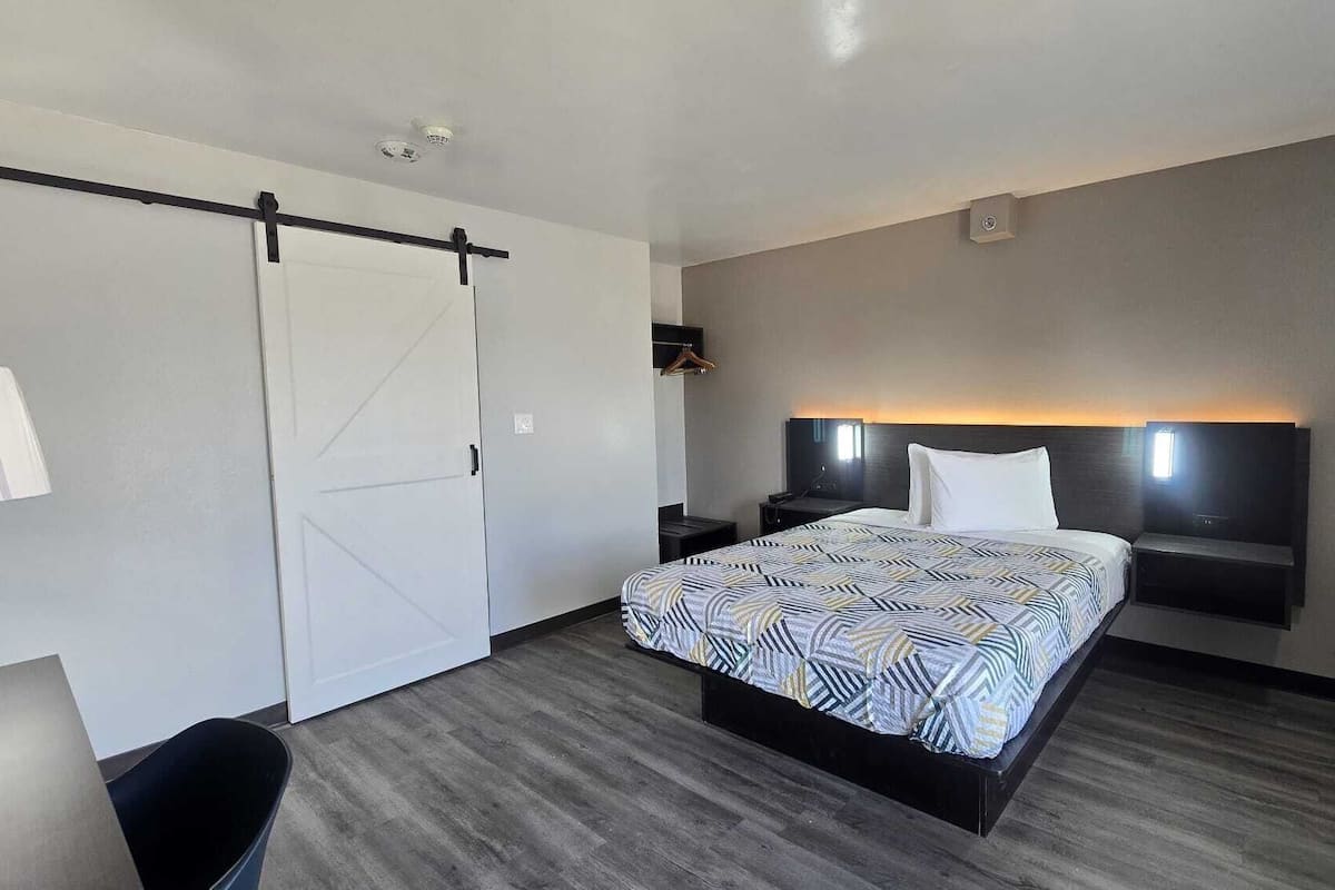 A hotel room with a bed, a desk, a chair, a wardrobe, and a wall-mounted TV.