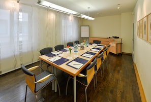 Una sala de conferencias con una larga mesa, sillas, un proyector y una pizarra.