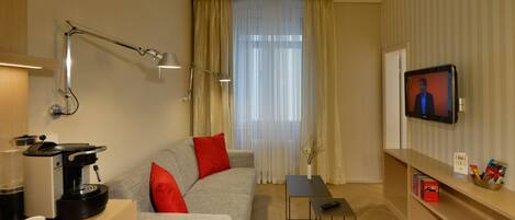 A modern living room with a sofa, a coffee machine, a TV, and a small table.