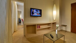 A modern living room with a flat-screen TV mounted on the wall, a coffee table with a remote control, and a bookshelf with books.