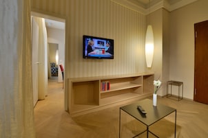 Una sala de estar moderna con un televisor de pantalla plana montado en la pared, una mesa de centro con un control remoto y una estantería llena de libros.