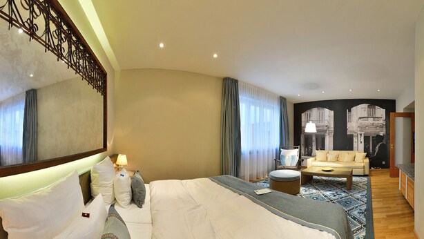 A hotel room with a large bed, a sofa, a coffee table, and a TV.