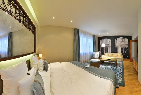 A hotel room with a large bed, a sofa, a coffee table, and a TV.