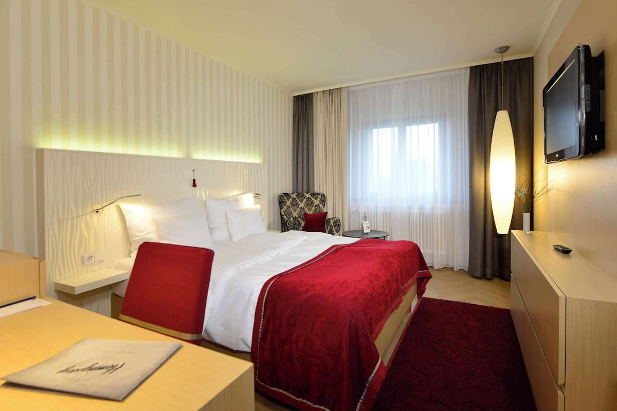 A hotel room with a large bed, a desk, a chair, a TV, and a window with curtains.