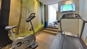 Un gimnasio moderno con cinta de correr, bicicleta estática y una televisión de pared mostrando un juego de billar.
