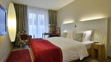 A hotel room with a large bed, a desk, a chair, and a nightstand.