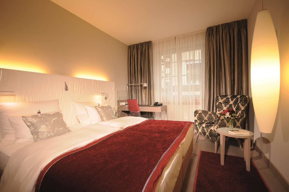 A hotel room with a bed, a desk, a chair, and a lamp.