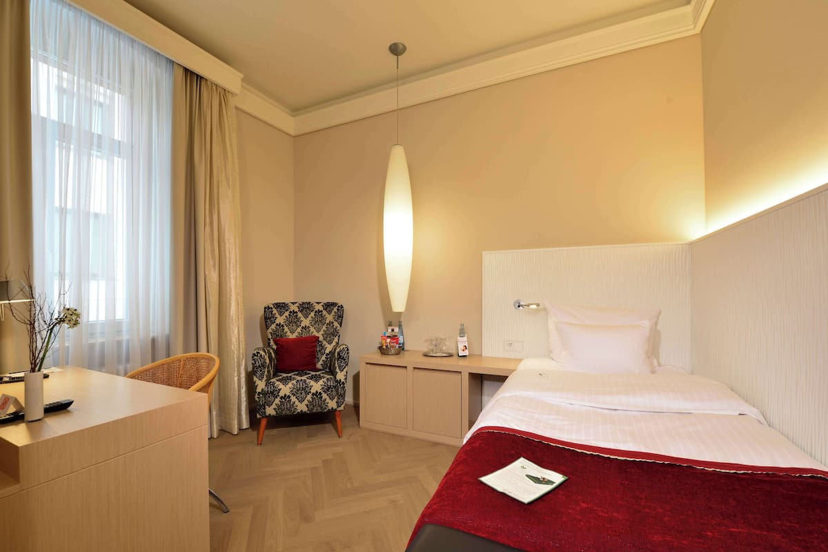 A hotel room with a bed, a desk, a chair, and a bedside table.