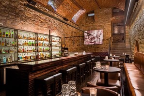 Un espace bar avec un mur en briques, des étagères remplies de bouteilles d’alcool et un écran de télévision.