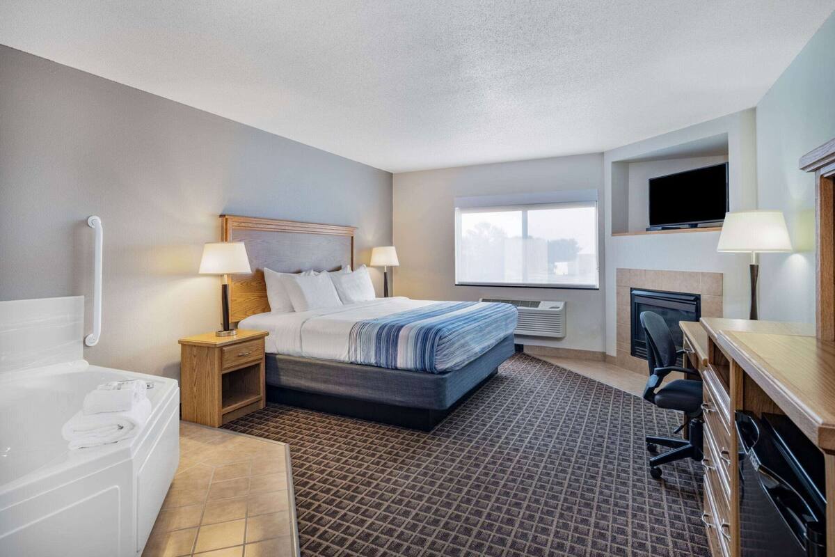 A hotel room with a bed, bedside lamps, a TV, a desk with a chair, a bathroom with a bathtub, and a window.