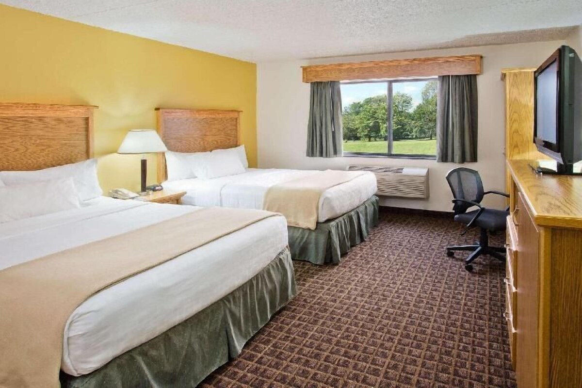 A hotel room with two beds, a desk with a chair, a television, and a window with curtains.