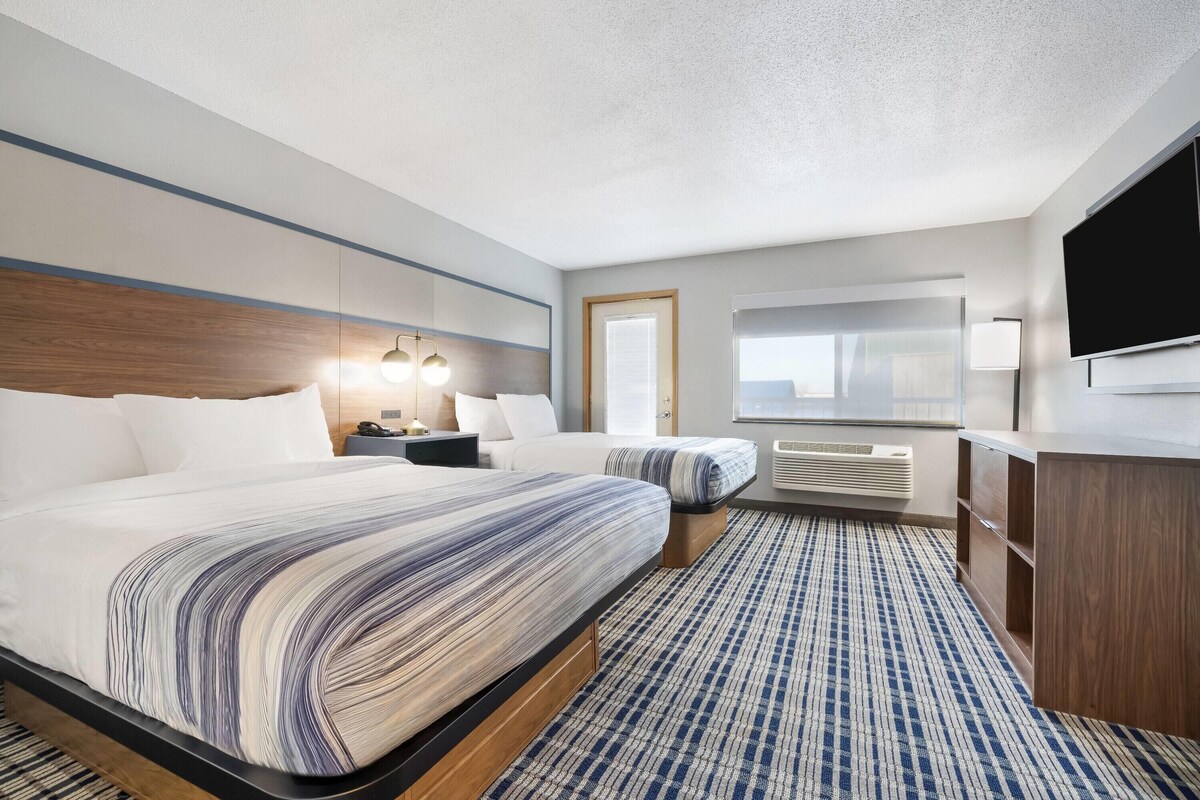 A hotel room with two beds, a flat-screen TV, a desk, and a large window.