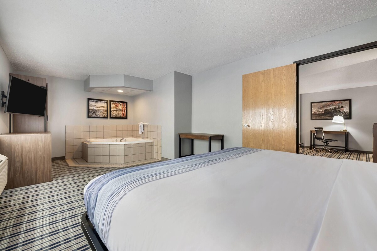 A hotel room with a large bed, a bathtub, a desk, and a TV.