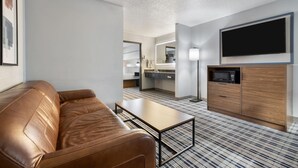 Una habitación de hotel moderna con un sofá de cuero, una pequeña mesa de centro, un televisor de pantalla plana en la pared, un microondas y una kitchenette compacta.