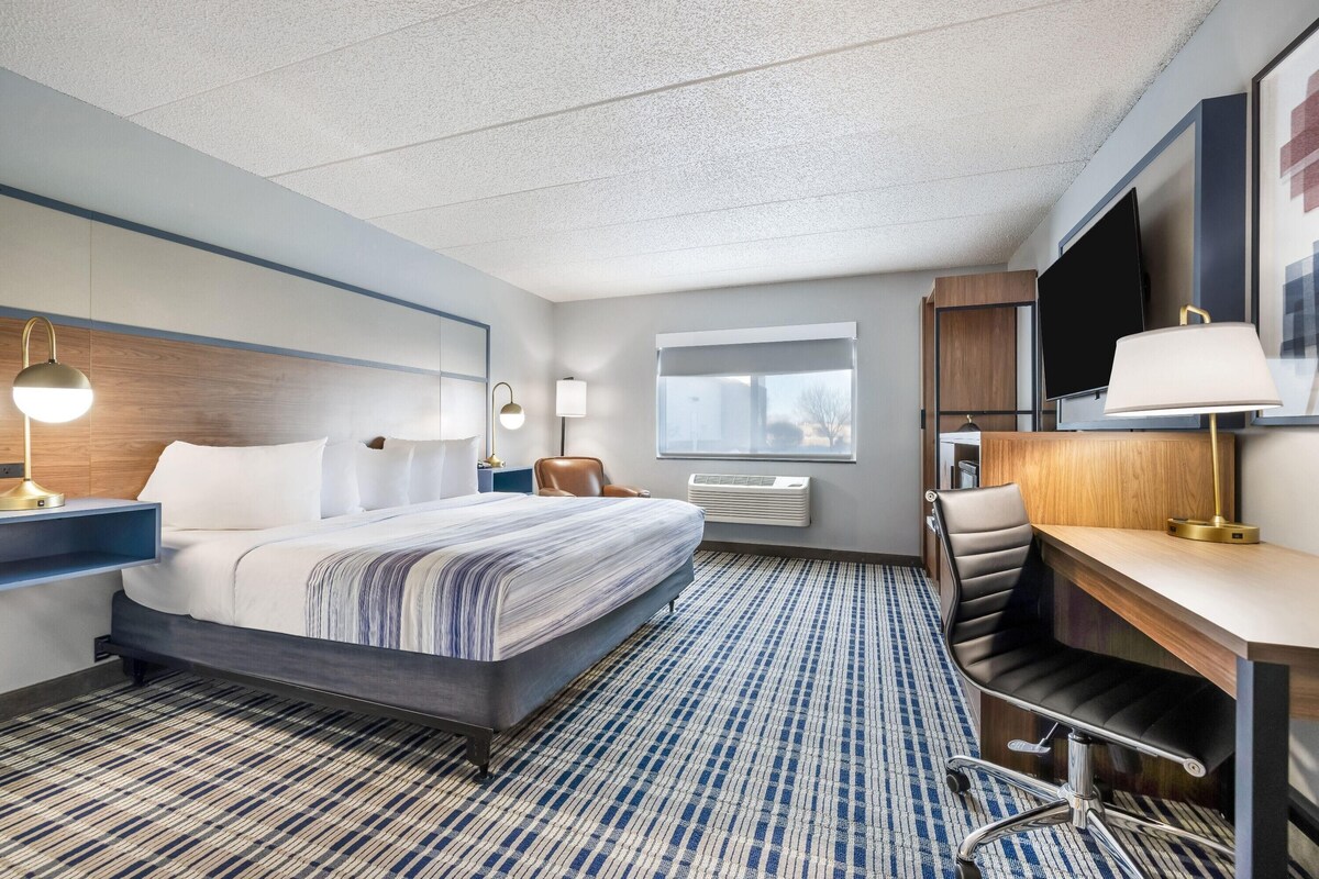 A hotel room with a bed, desk, chair, TV, and window.