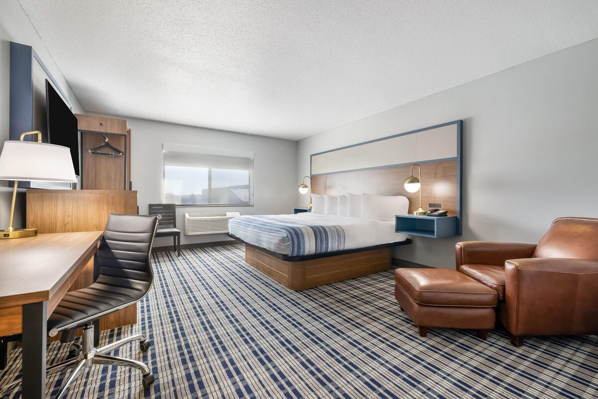 A hotel room with a bed, desk, chair, and a large mirror.