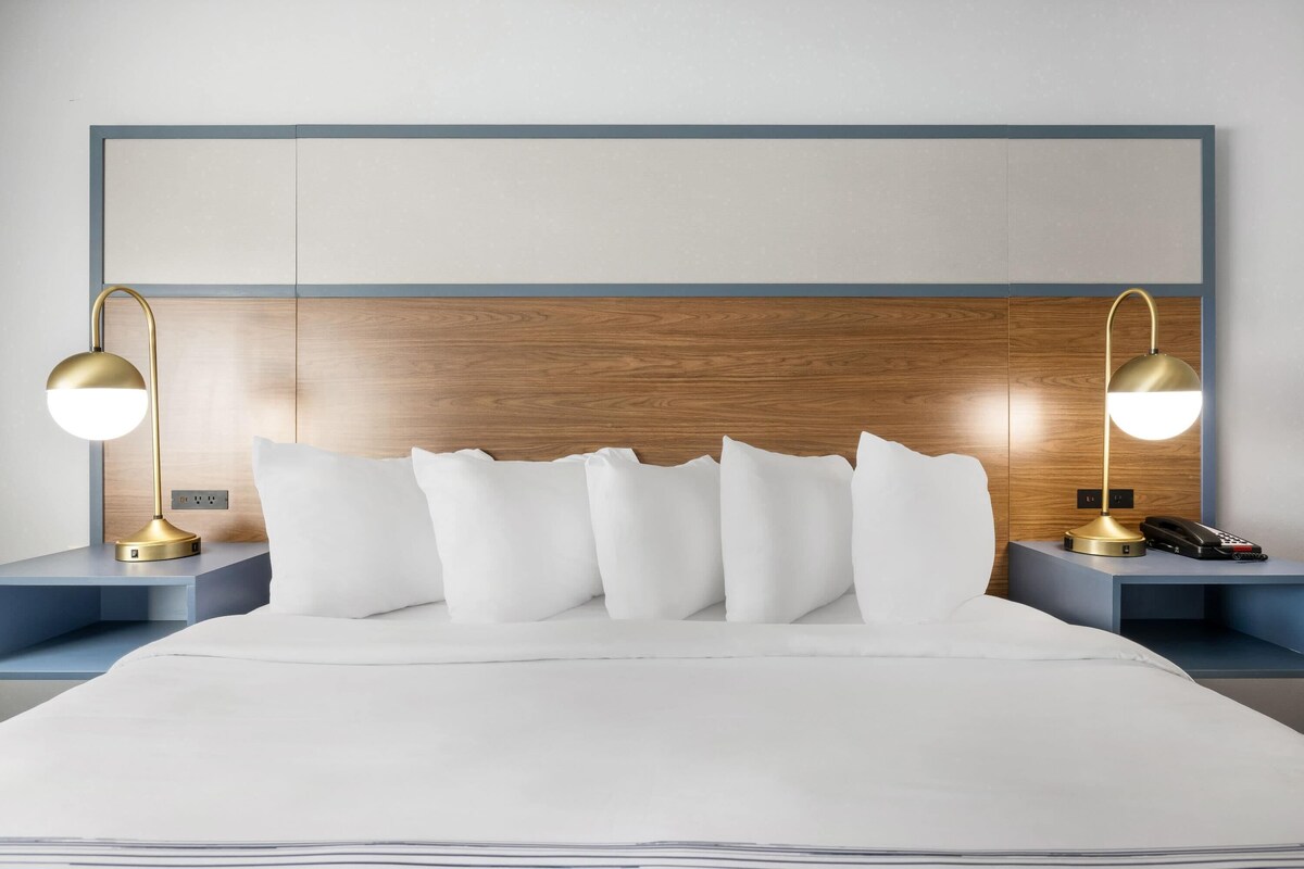 A hotel room with a wooden headboard, a bed with white bedding, two bedside tables with lamps, and a telephone.