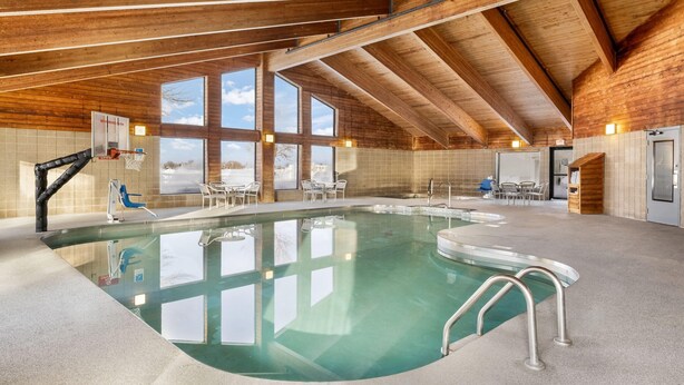 Una piscina interior con techo de madera, paredes de vidrio transparente y aro de baloncesto.